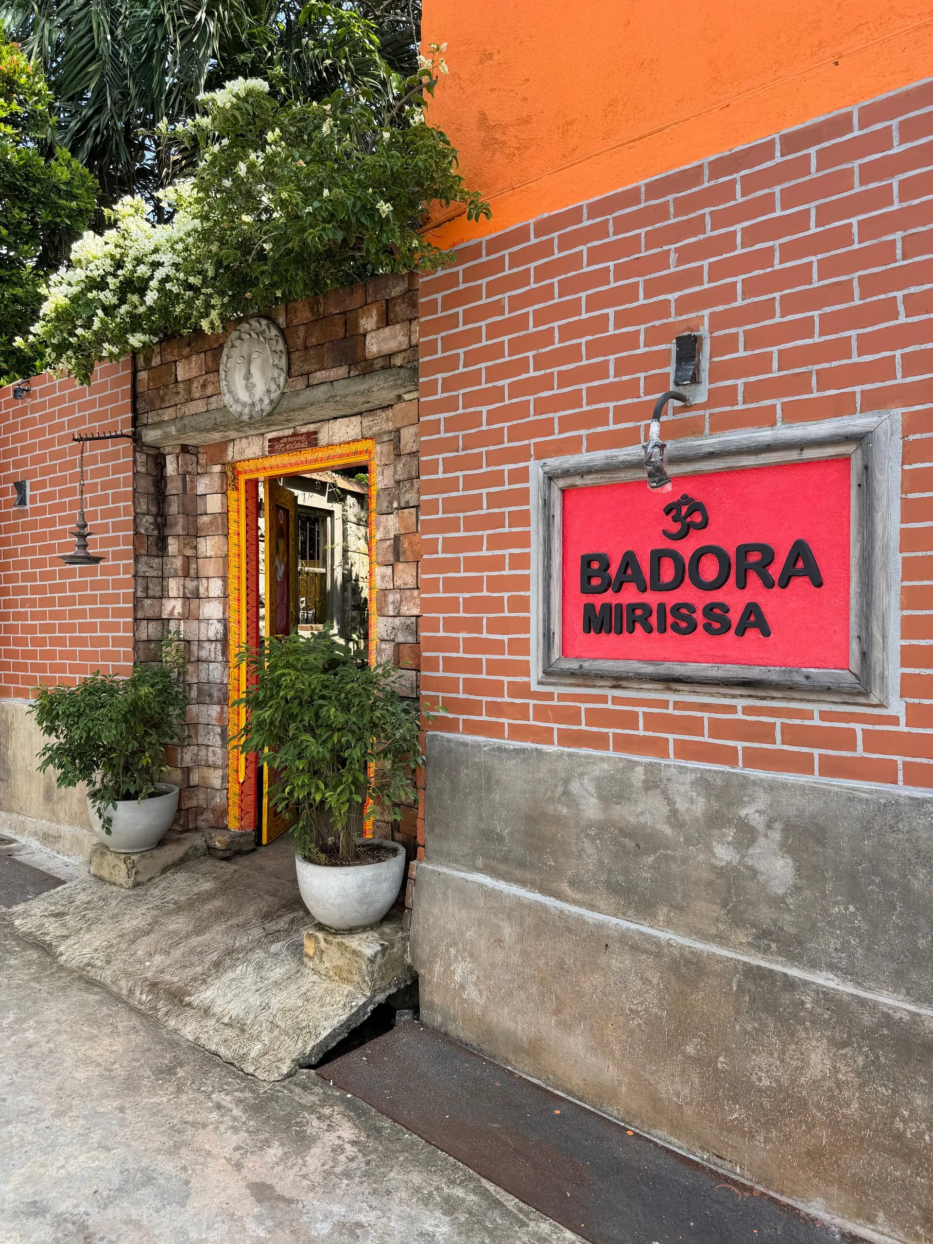 The entrance to Badora Spa in Mirissa — a red sign on the brick wall and an arched doorway hung with marigolds