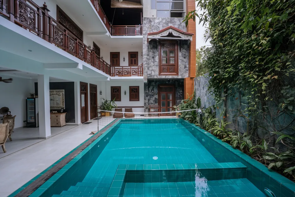 The main villa inner courtyard: turquoise pool with a volleyball net, carved timber balconies on the floors above and a creeper-covered stone wall