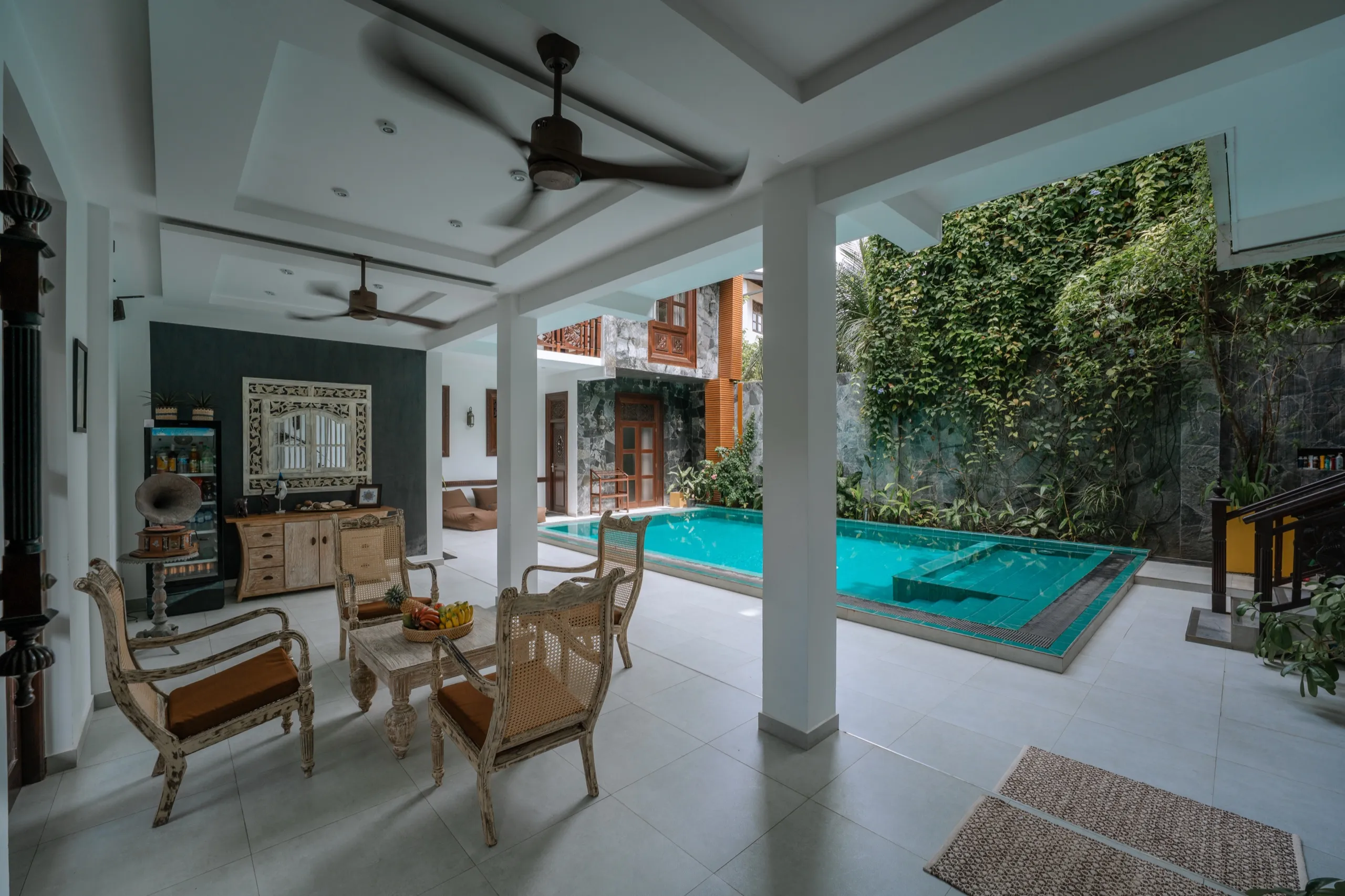 Cane armchairs around a small table beside the turquoise courtyard pool of the main villa, a creeper-covered stone wall behind
