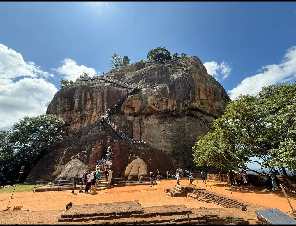 The Sigiriya rock fortress above the plain, the lion's paws and the stairway with visitors climbing at its foot