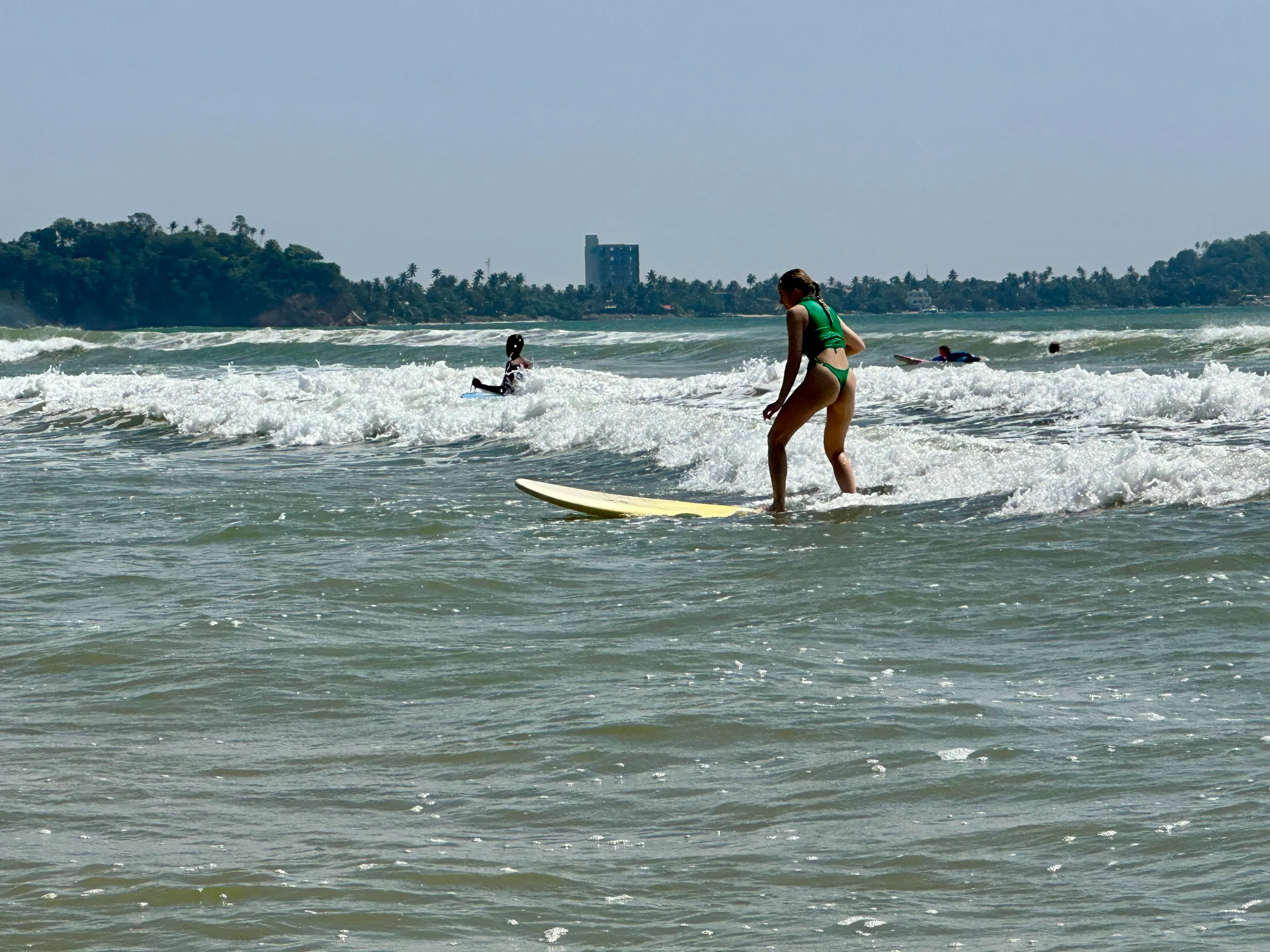 A surfer carrying a longboard through the shallows at Weligama Bay