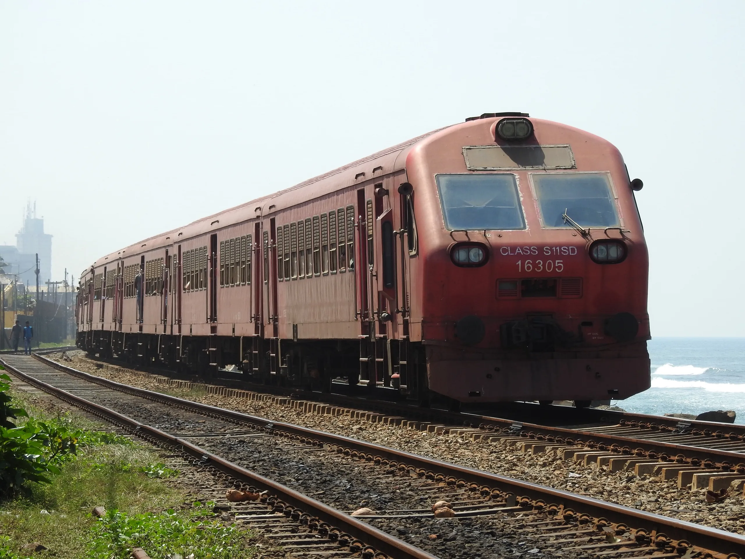 A red Sri Lanka Railways coastal-line train leaving Kollupitiya station in Colombo, the Indian Ocean right beside the tracks
