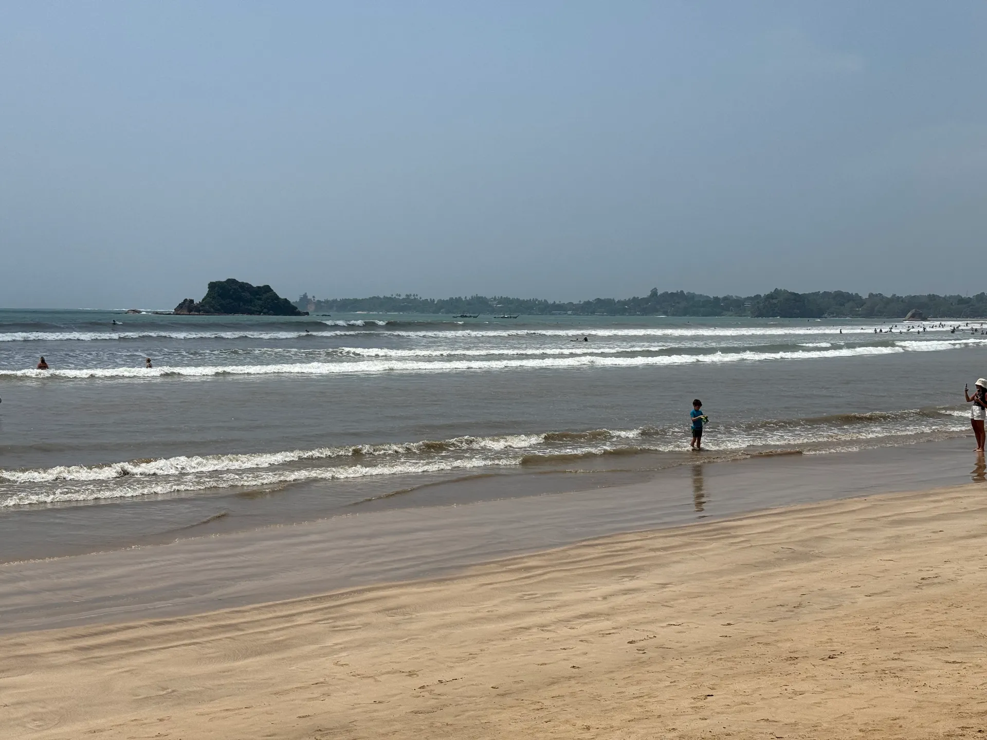 Wide sand and gentle surf on Sri Lanka's southern coast, with a rocky islet offshore